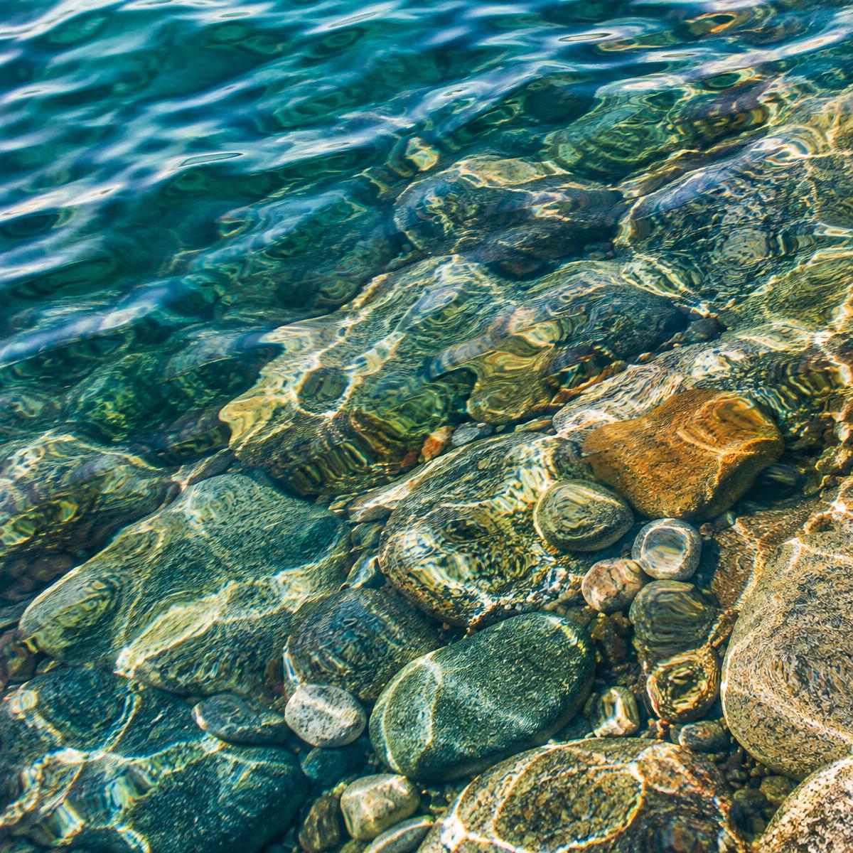 Sunlit lake water over smooth pebbles